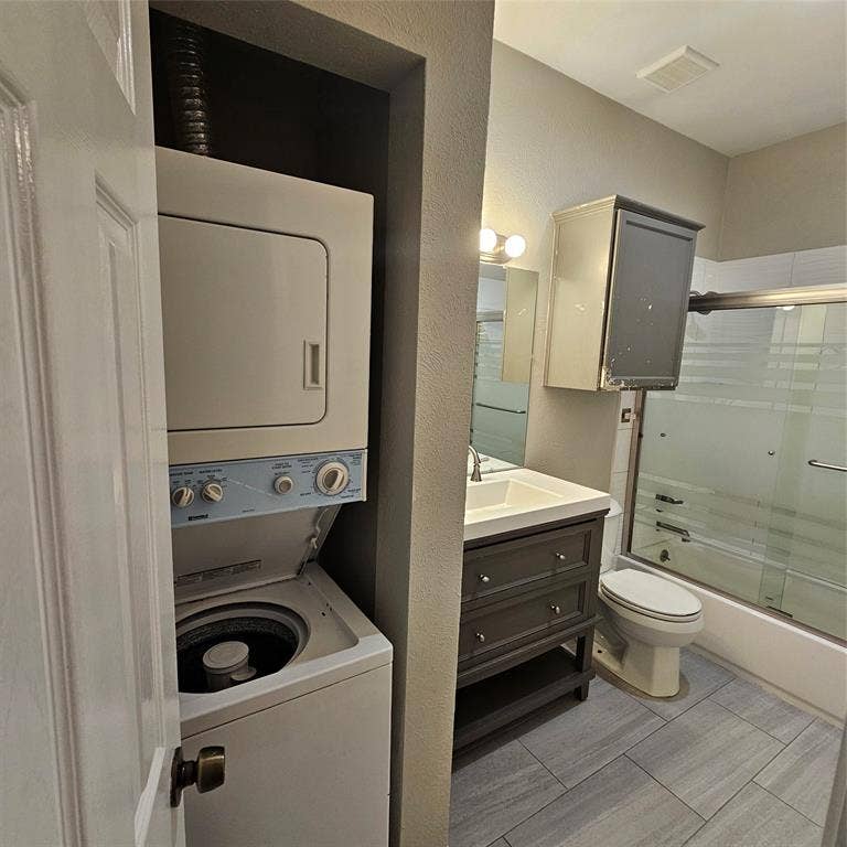 9600 ROYAL, #612, Dallas, TX 75243 Full bathroom featuring estacked washer and dryer, shower / bath combination with glass door, vanity, and a textured wall