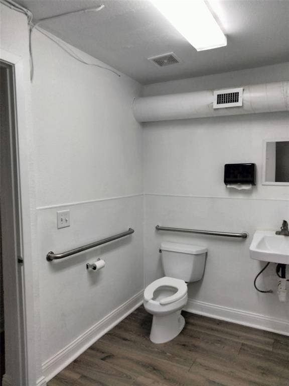 513 N 4th Street, Princeton, TX 75407 Restroom featuring wood-finish flooring, white wainscoting, wall-mounted sink, and grab bars