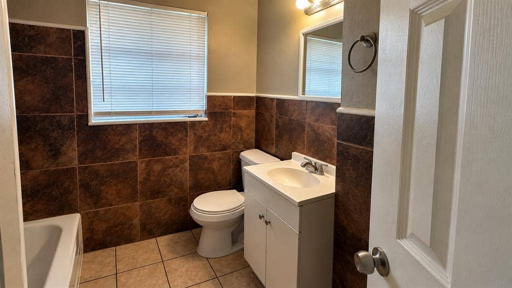 914 Harlandale Avenue, Dallas, TX 75216 Full bathroom featuring a single vanity, a toilet, a bathtub, and brown-toned tile wainscoting