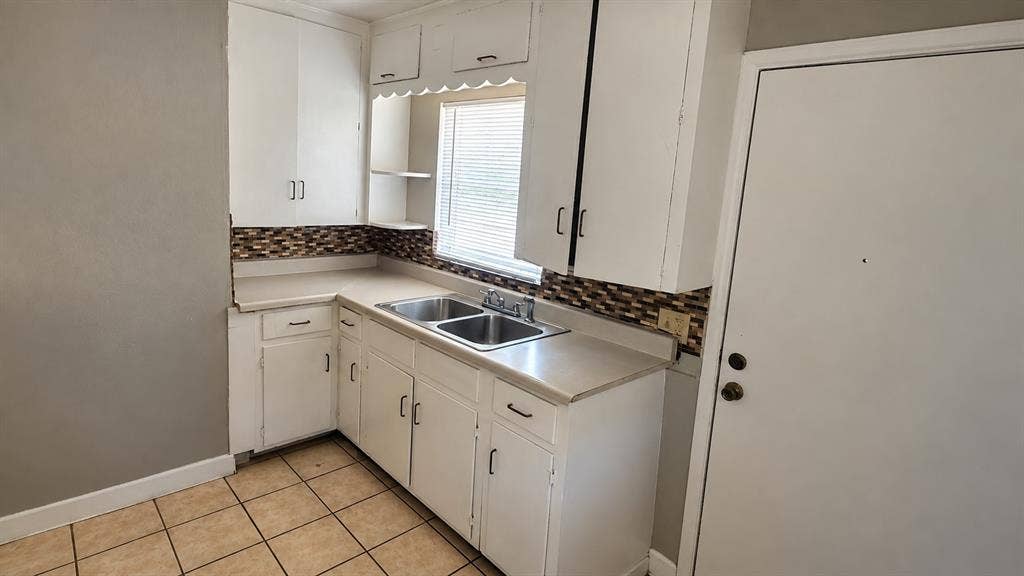 914 Harlandale Avenue, Dallas, TX 75216 Kitchen featuring white cabinetry, a double basin stainless steel sink, a mosaic tile backsplash, and light-toned tile flooring