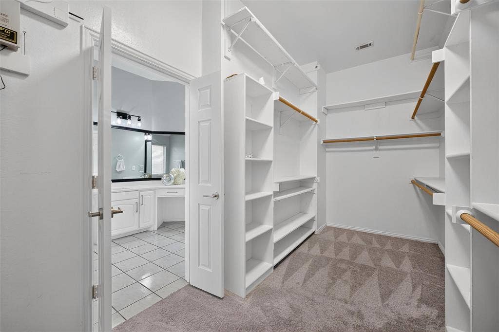 1102 Hartman Court, Arlington, TX 76006 Walk-in closet featuring extensive built-in shelving, multiple hanging rods, and patterned carpet flooring