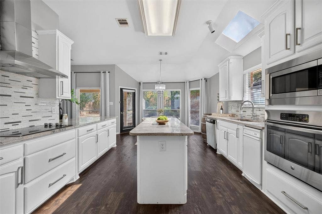 1102 Hartman Court, Arlington, TX 76006 Kitchen featuring white cabinetry, stainless steel appliances, a center island with countertop, hardwood-finish flooring, and a skylight