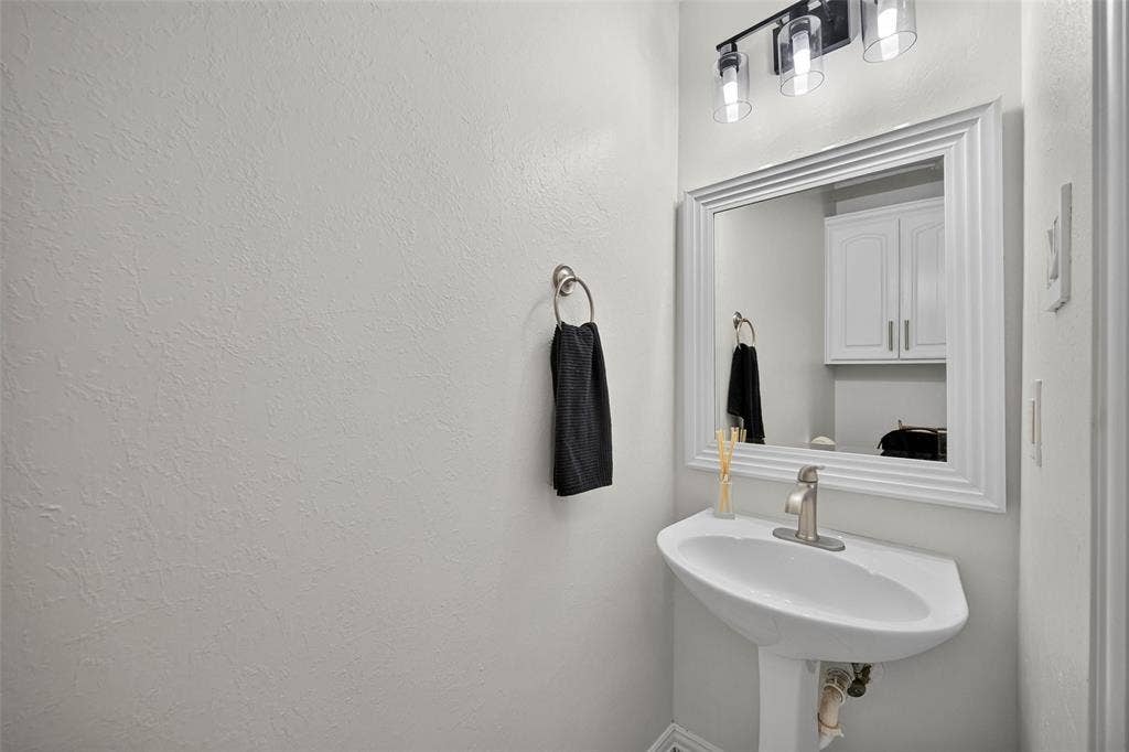 1102 Hartman Court, Arlington, TX 76006 Pedestal sink with a single-handle faucet, framed mirror, and a three-light vanity fixture