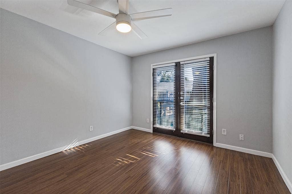 10207 Regal Oaks Drive, #210, Dallas, TX 75230 Wood-finish flooring, light gray wall finish, white ceiling fan with integrated lighting, and dark-framed double doors with horizontal blinds
