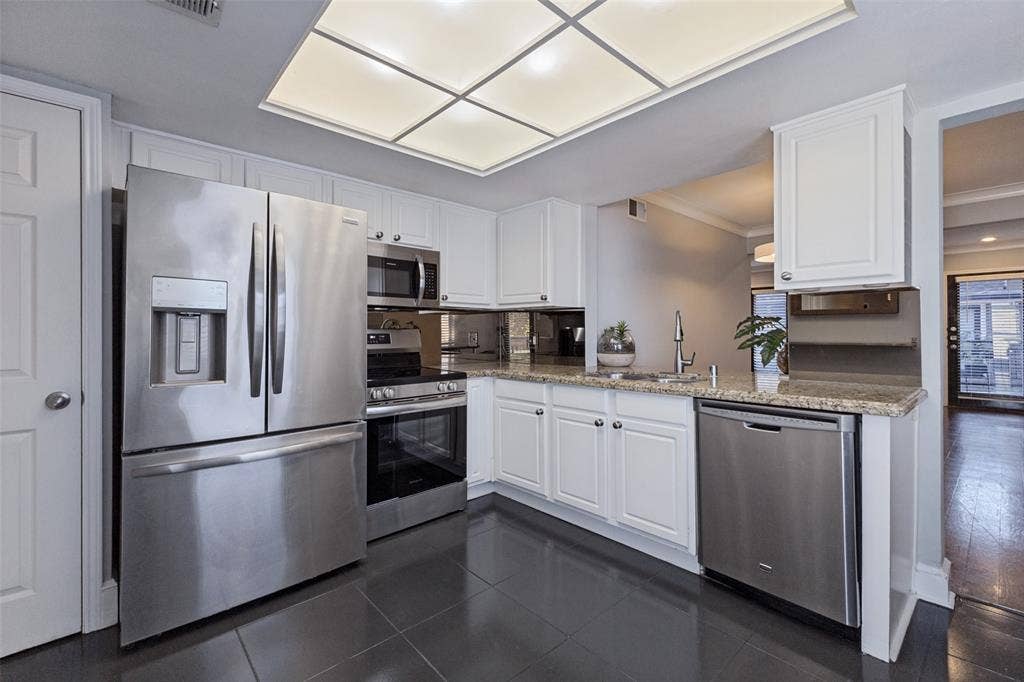 10207 Regal Oaks Drive, #210, Dallas, TX 75230 Kitchen featuring white cabinetry, stainless steel appliances, granite countertops, and dark tile flooring