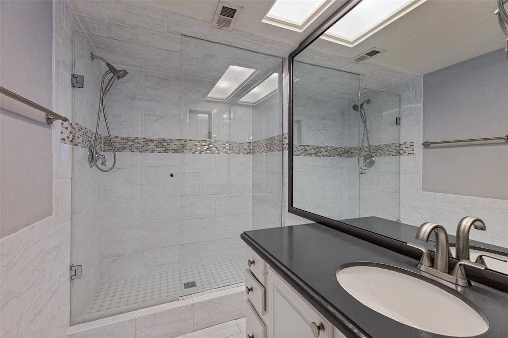 10207 Regal Oaks Drive, #210, Dallas, TX 75230 Glass-enclosed shower with white tiled walls and mosaic accent
