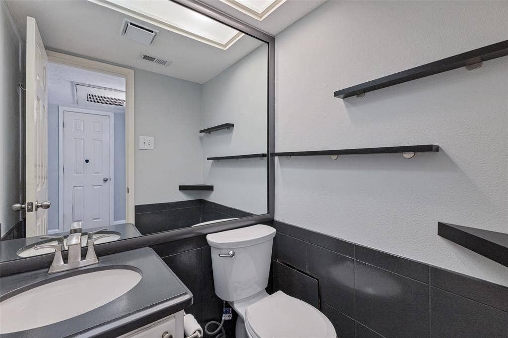 10207 Regal Oaks Drive, #210, Dallas, TX 75230 Recessed lighting, wood-finish floating shelves, full-width vanity mirror, compact toilet, and a vanity with an integrated sink