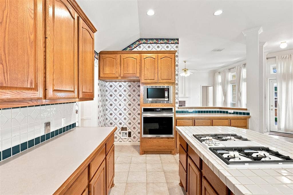 3617 Mackenzie Lane, Richardson, TX 75082 Wood cabinetry with stainless steel built-in appliances, tile backsplash, and a tile-top island with a cooktop.