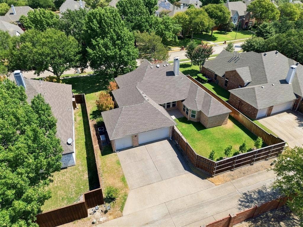 3617 Mackenzie Lane, Richardson, TX 75082 Aerial View showing brick exterior with an attached two-car garage, concrete driveway, and gabled roof, and green grass.