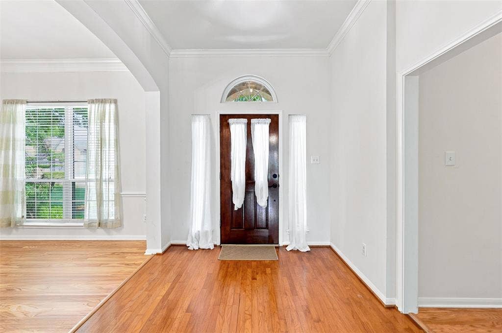 3617 Mackenzie Lane, Richardson, TX 75082 Entryway featuring wood-finish flooring, a wood paneled door with an arched transom, and white wall finishes.