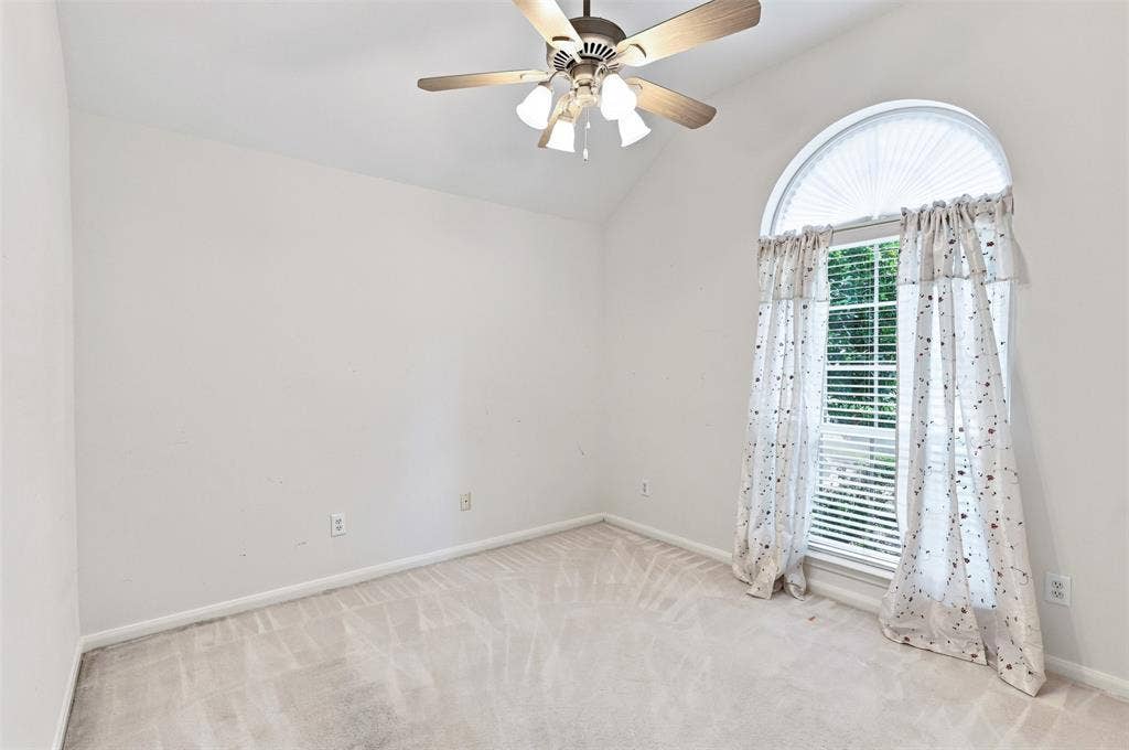 3617 Mackenzie Lane, Richardson, TX 75082 Secondary bedroom with vaulted ceiling with an attached ceiling fan, arched window with horizontal blinds, and neutral carpet flooring.