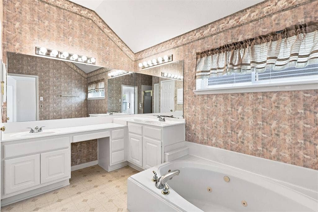 3617 Mackenzie Lane, Richardson, TX 75082 Primary bathroom features dual vanity sinks with white cabinetry, mirrored wall, recessed jetted bathtub, and patterned wallpaper.