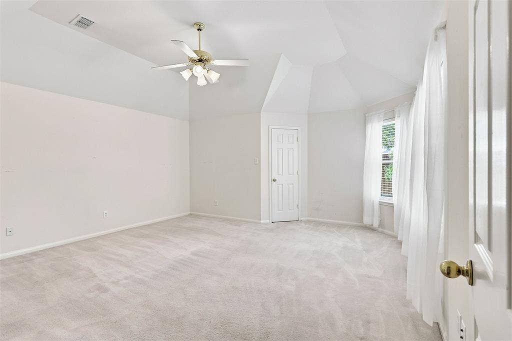 3617 Mackenzie Lane, Richardson, TX 75082 Primary bedroom features vaulted ceilings, carpeted flooring, ceiling fan with integrated lighting, paneled door, and a multi-pane window.