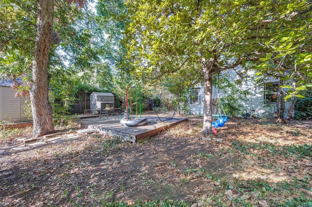 559 Blanning Drive, Dallas, TX 75218 Expansive backyard featuring mature trees, a wooden patio, and two storage sheds
