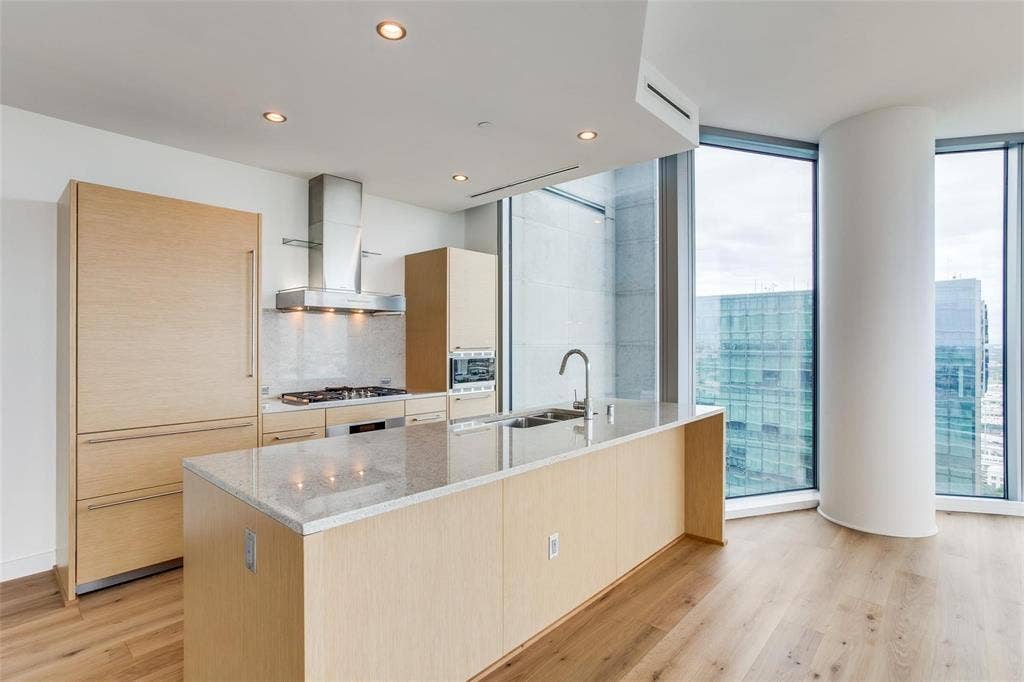 Gourmet kitchen featuring a large island with sink, stainless steel appliances, wood-finish cabinetry, and recessed lighting