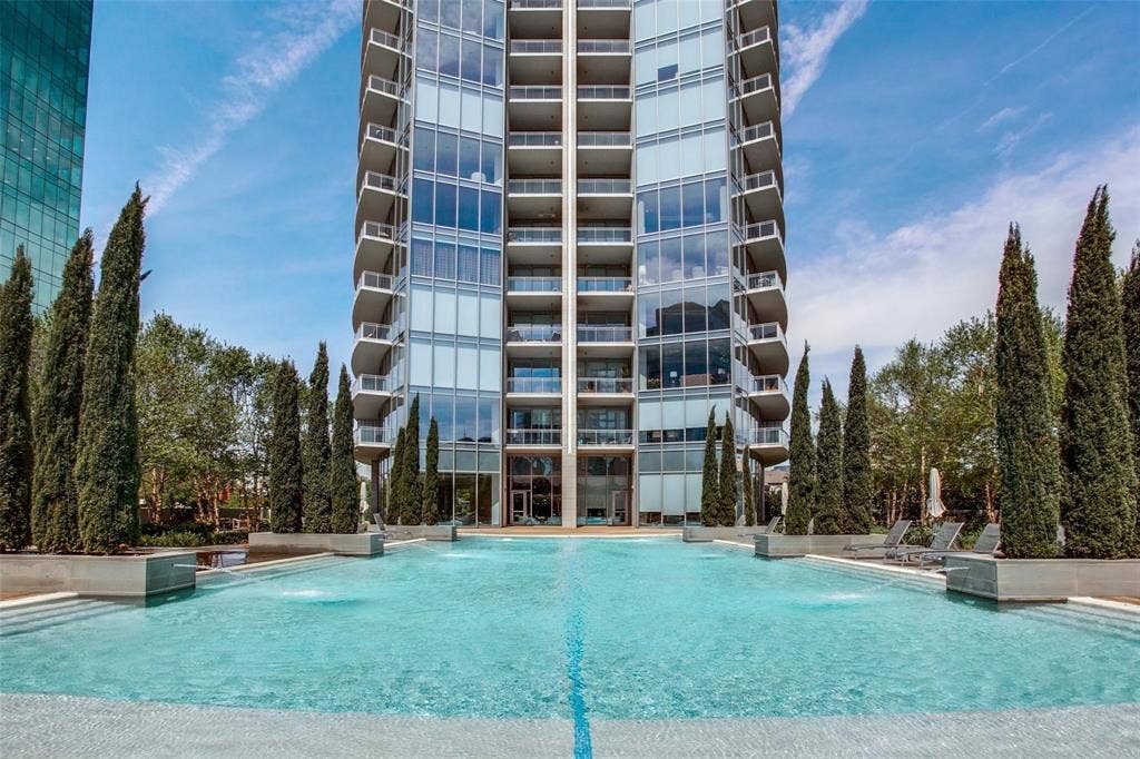 Outdoor pool area featuring water features, concrete decking, and columnar evergreen plantings