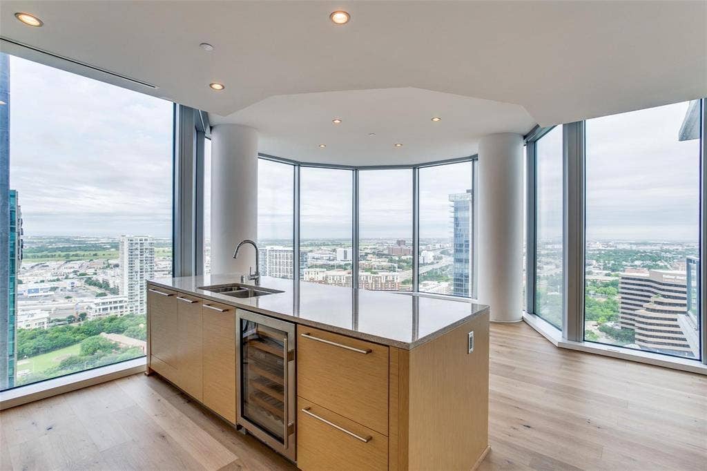 Expansive floor-to-ceiling windows, island with integrated sink, stainless steel wine refrigerator, recessed lighting, and wood-finish flooring