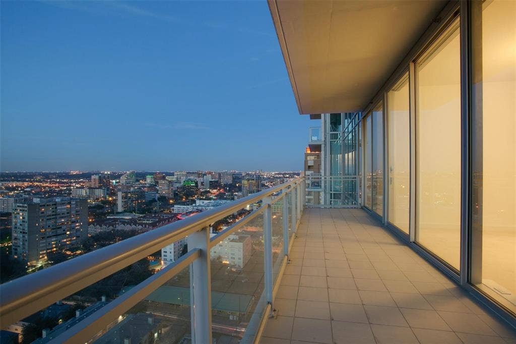 Expansive balcony featuring a tiled floor, clear glass railings, and a wide sliding glass door entry