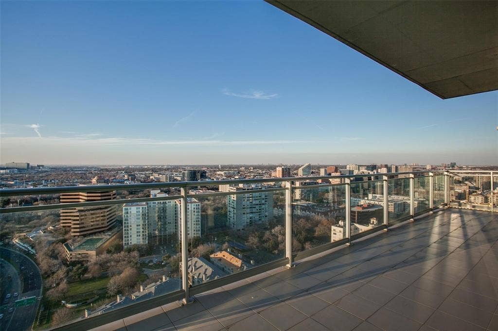 Expansive balcony featuring glass railings, tiled flooring, and an urban cityscape