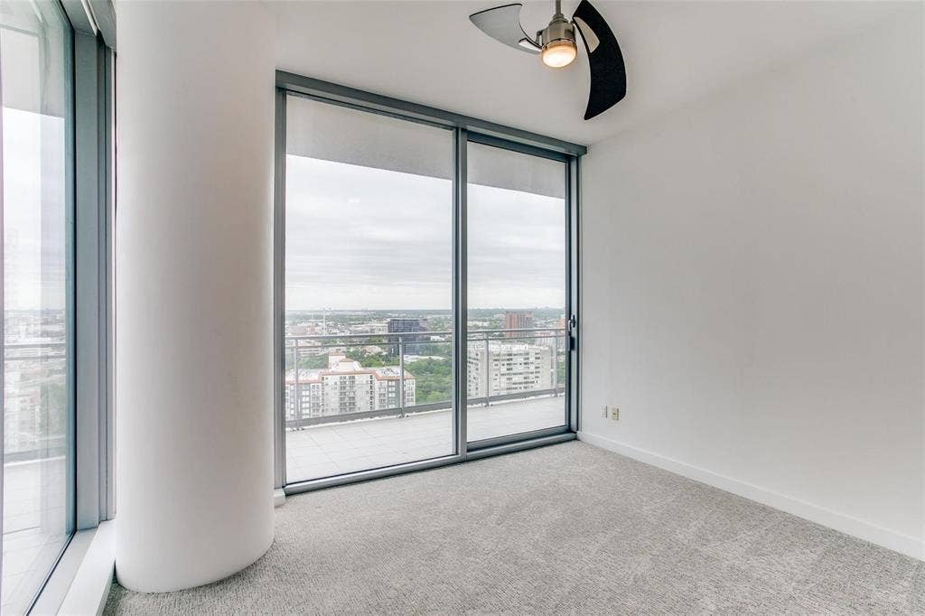 Floor-to-ceiling windows with roller shades, a private balcony, contemporary ceiling fan, and light grey carpet