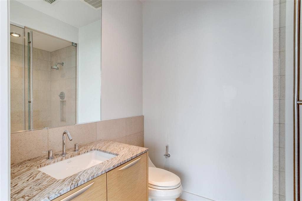 Vanity with a polished stone countertop, undermount sink, and wood-finish cabinetry