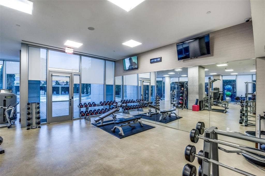 Fitness center featuring concrete flooring, full-height windows with roller shades, mirrored walls, and flush-mounted ceiling lighting