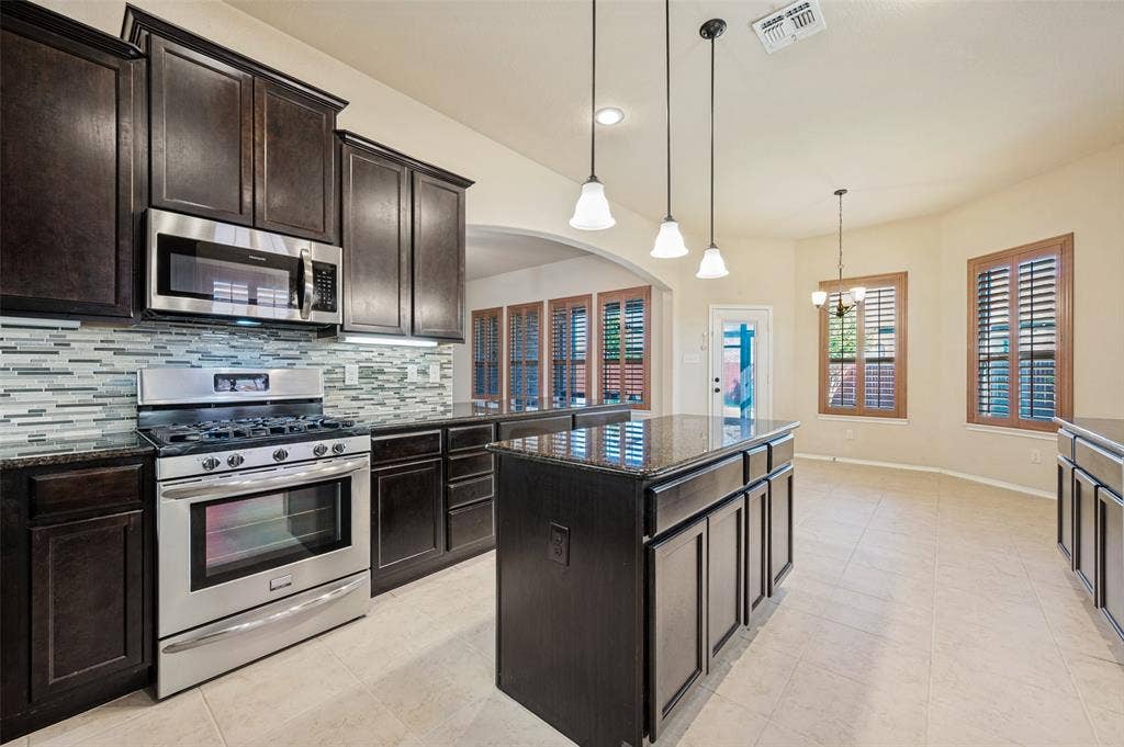 Kitchen featuring dark wood cabinetry, stainless steel appliances, a mosaic tile backsplash, and a central island with a stone countertop