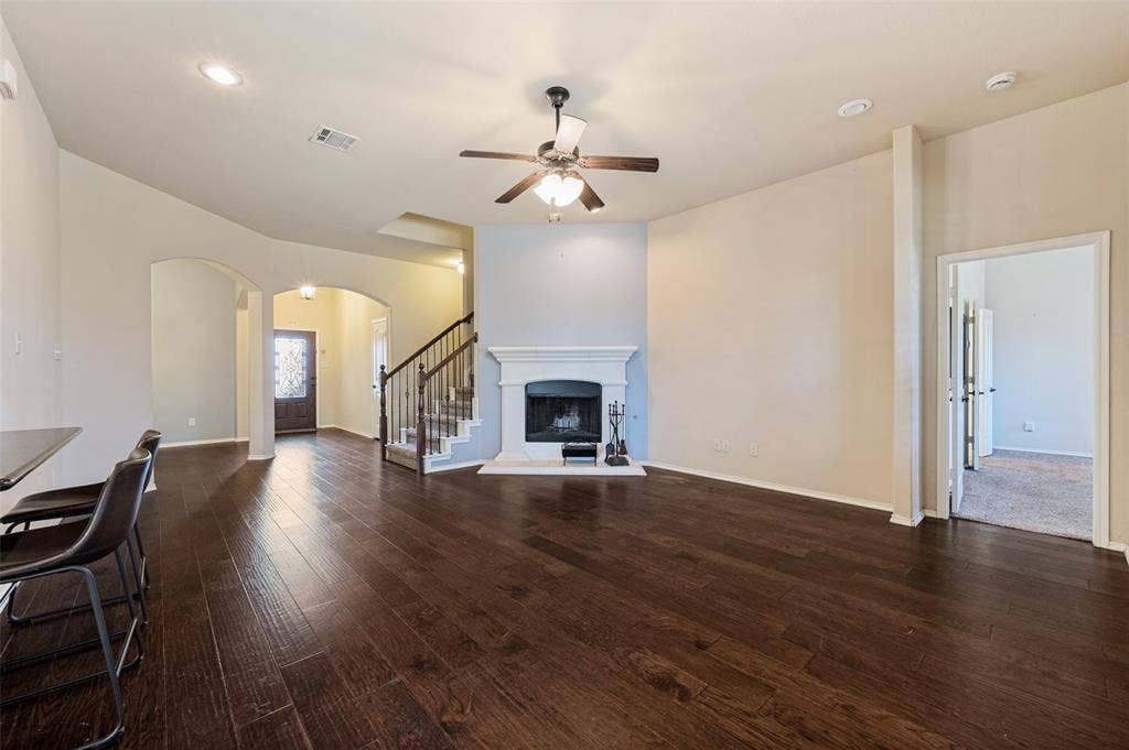 Wood-finish flooring throughout, a white fireplace with a mantel, a ceiling fan with integrated lighting, recessed lighting, and an arched entry
