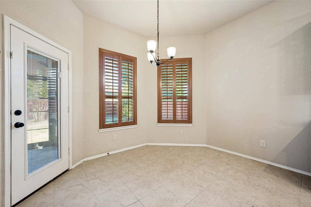 Tiled flooring, two windows with wood-finish plantation shutters, ceiling-mounted light fixture, and a glass-paneled door