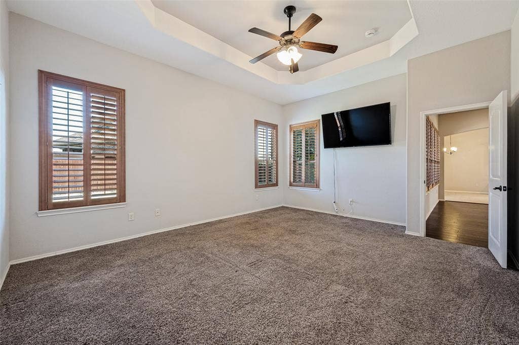 Tray ceiling with a ceiling fan, two windows with wood-finish shutters, and wall-to-wall carpeting