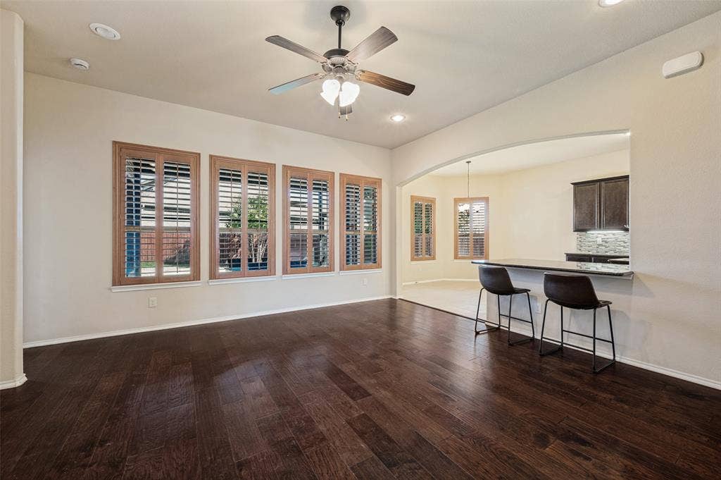 Wood-finish flooring, plantation shutters, ceiling fan with light fixture, recessed lighting, and a breakfast bar with stone-look countertop