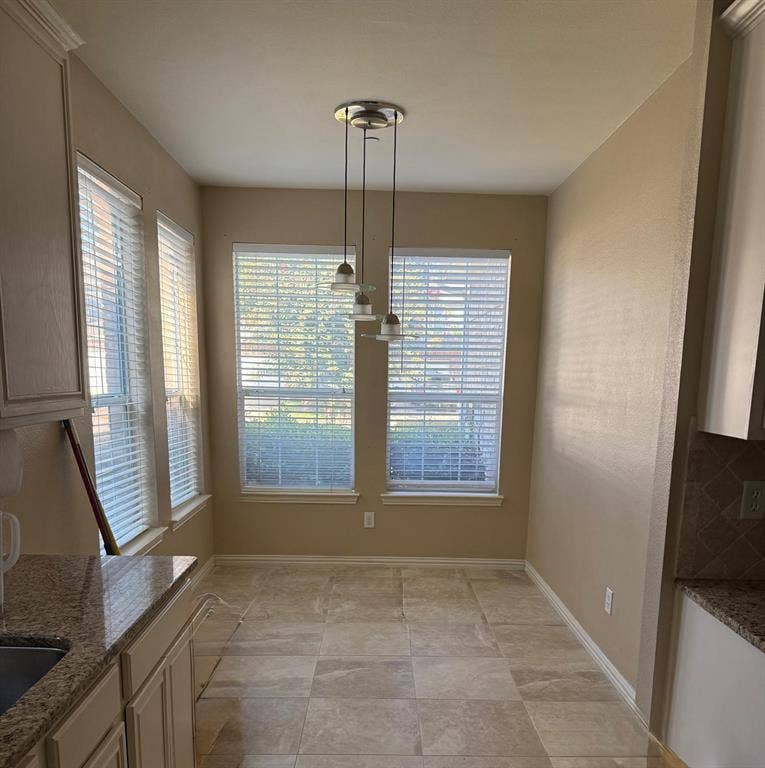 10012 Castlewood Drive, Plano, TX 75025 Recessed dining nook featuring ceramic tile flooring, three large windows with blinds, a multi-light pendant fixture, and a granite-topped counter with an undermount sink