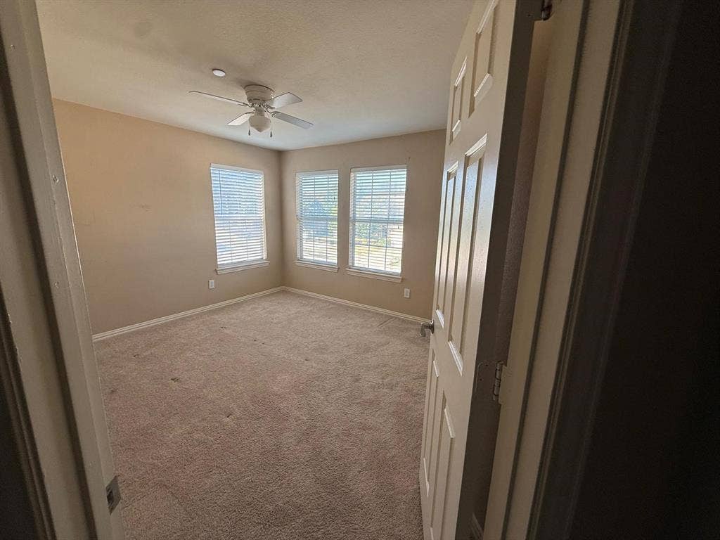 10012 Castlewood Drive, Plano, TX 75025 Carpeted room featuring a ceiling fan, three windows with blinds, and neutral painted walls