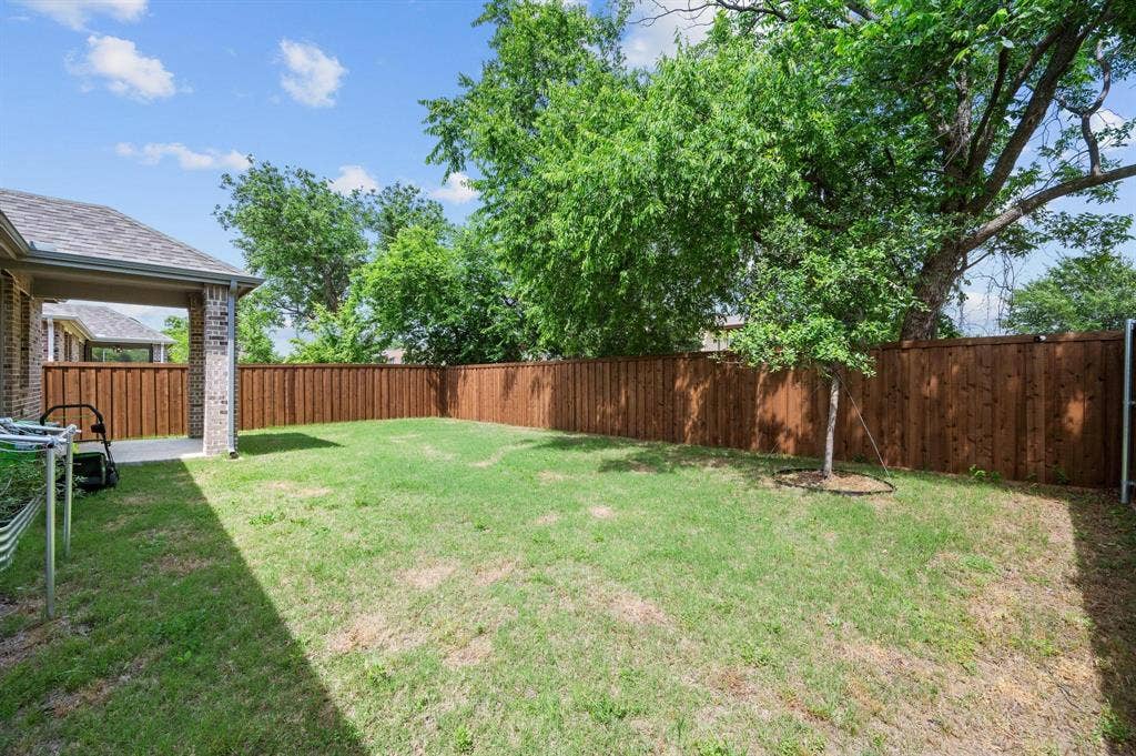 Expansive fenced backyard featuring a covered patio, brick columns, and mature trees