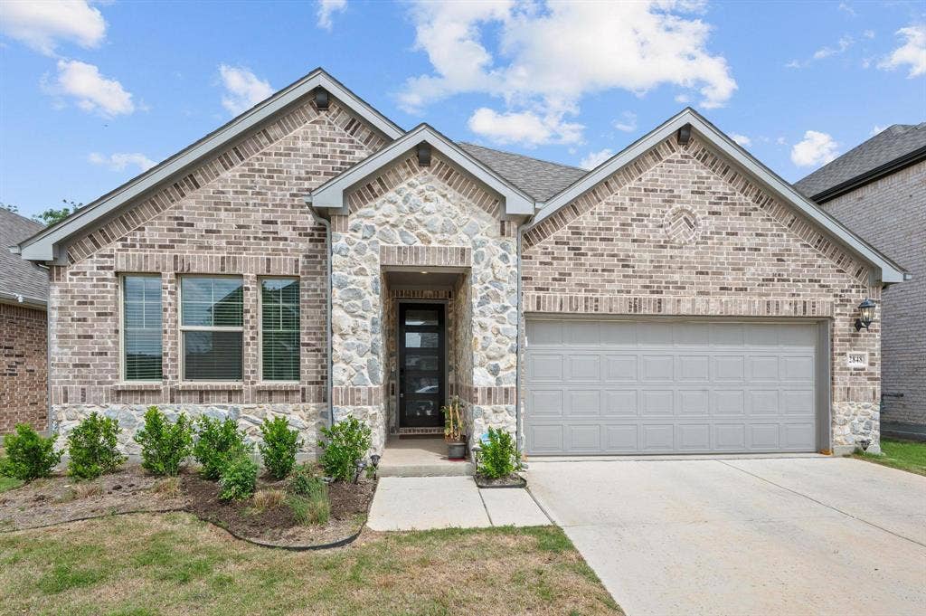 Brick and stone exterior with an attached garage, paved driveway, and established landscaping