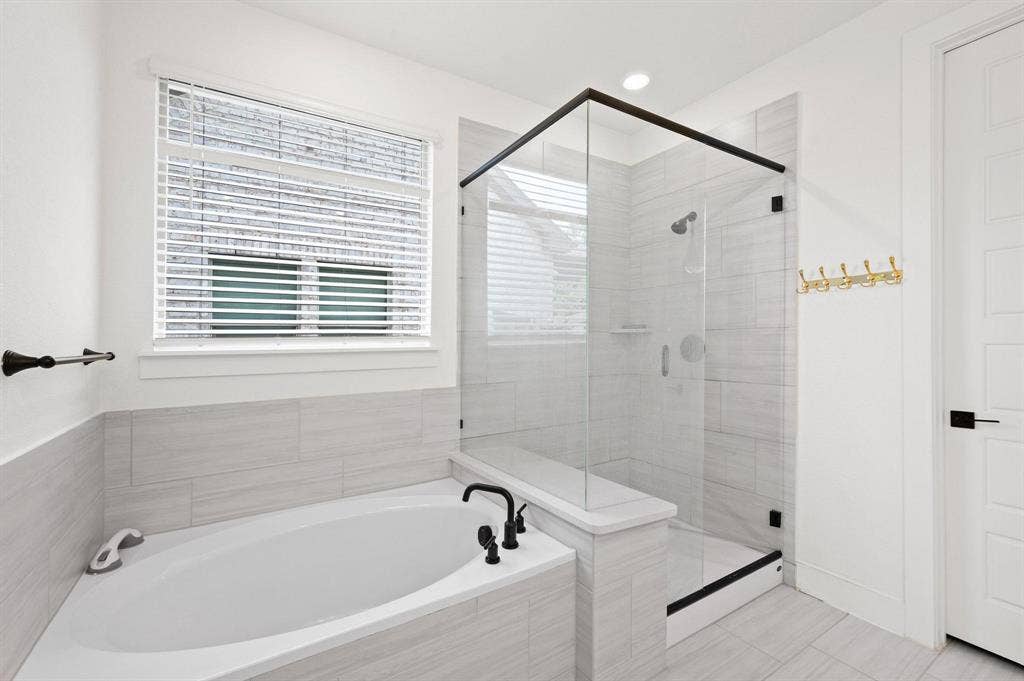 Built-in corner tub with black fixtures, walk-in shower with glass enclosure, tiled shower walls, and a recessed shower shelf