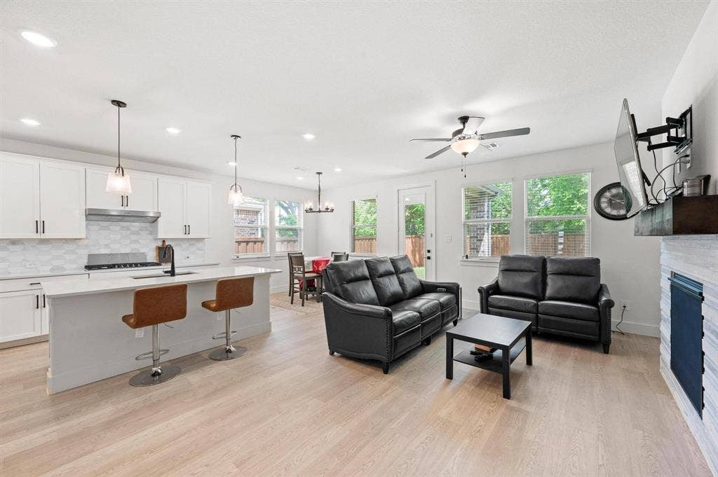 Open-concept living space featuring wood-finish flooring, a kitchen island with pendant lighting, white cabinetry, a tile backsplash, and a ceiling fan