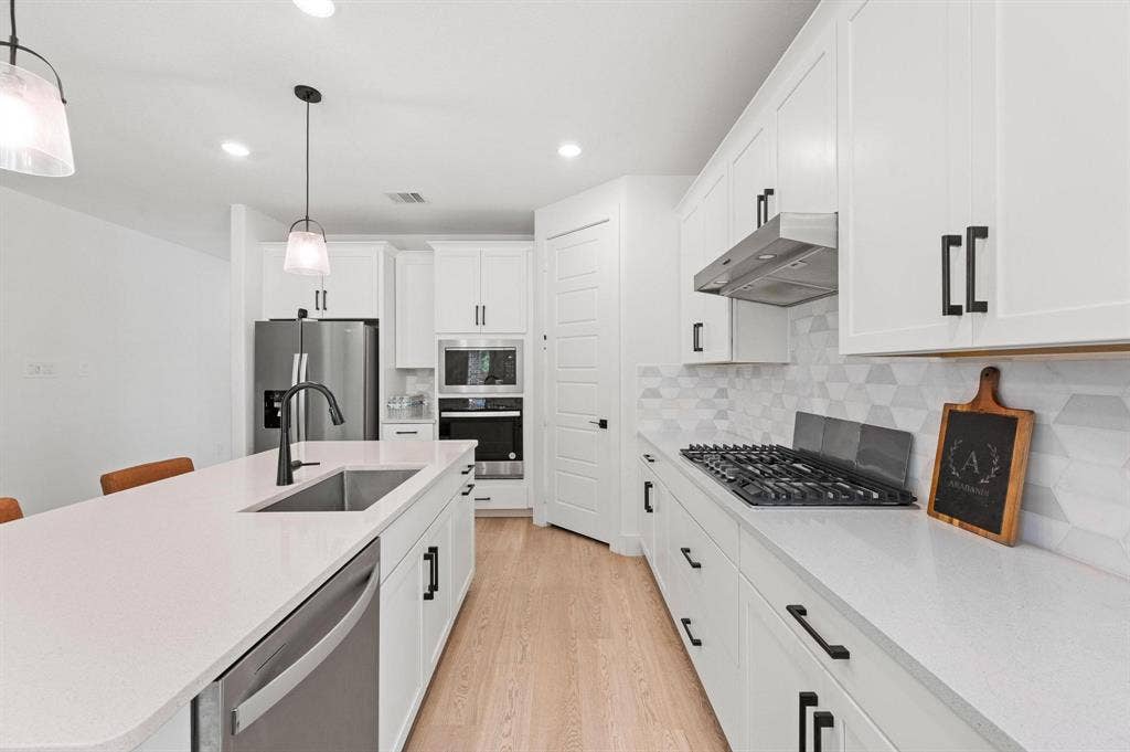 White kitchen cabinetry with black hardware, light wood-finish flooring, stainless steel appliances, and a gas range