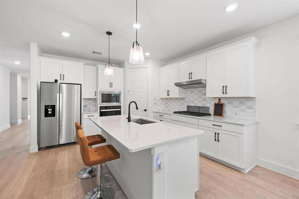 Kitchen featuring a central island, stainless steel appliances, white cabinetry with black hardware, white countertops, and wood-finish flooring