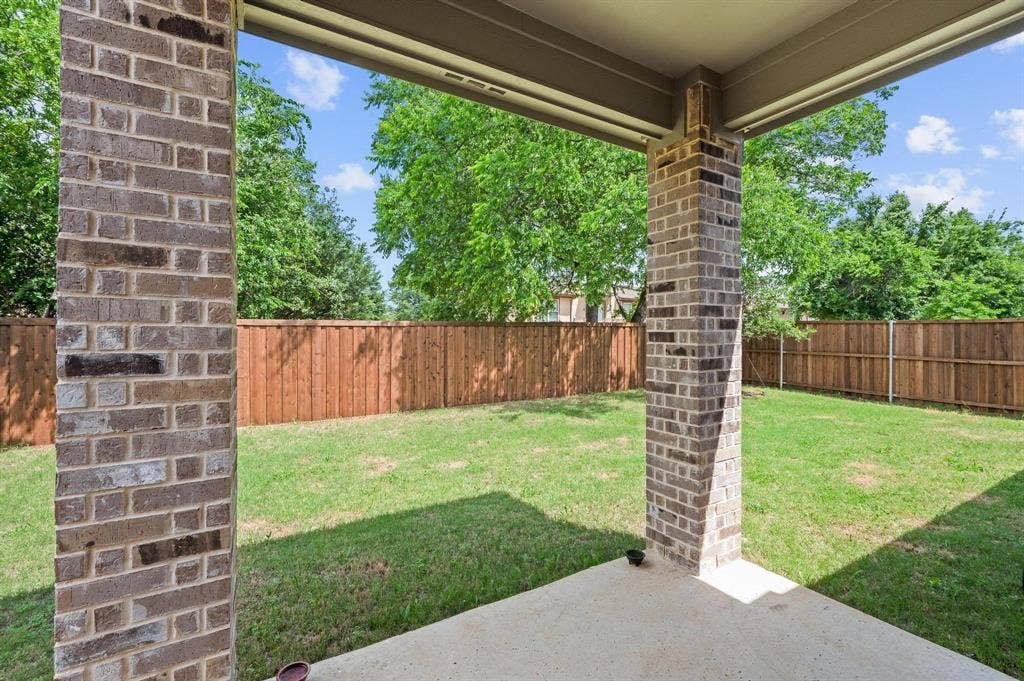 Covered patio with a concrete surface, brick columns, and a fully fenced backyard featuring a grassy lawn and mature trees