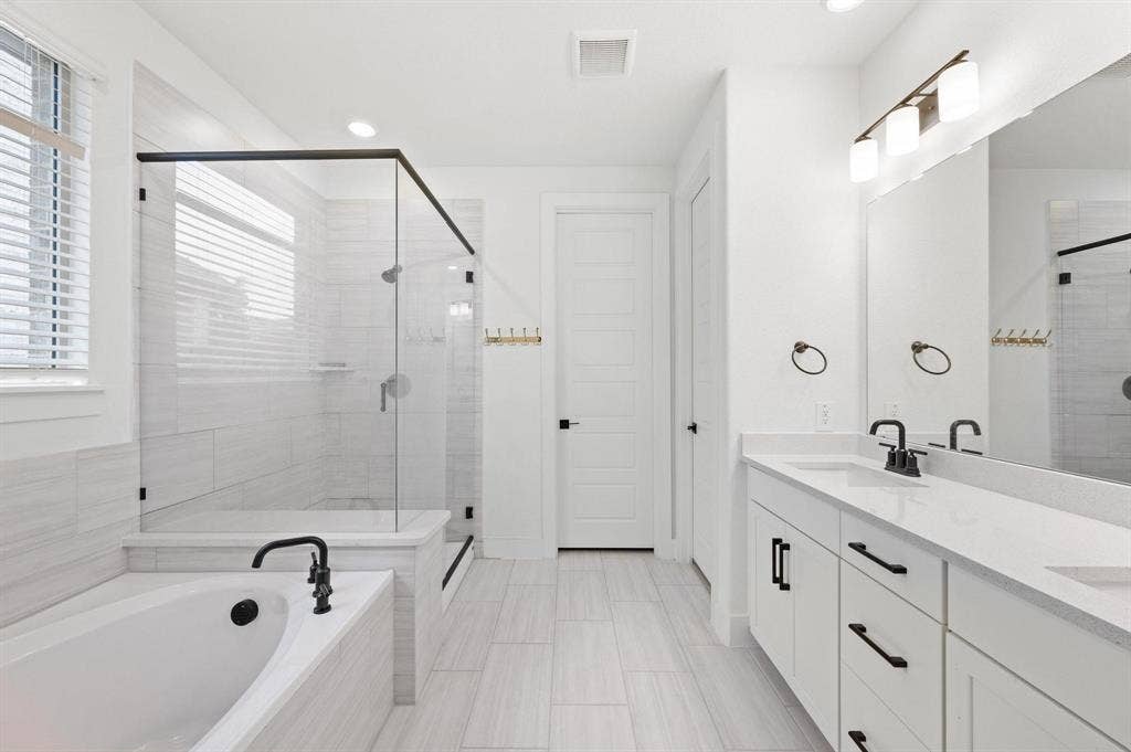 Dual vanity with quartz countertops, a soaking tub with black fixtures, a walk-in shower with clear glass enclosure, white tile flooring, and white paneled doors