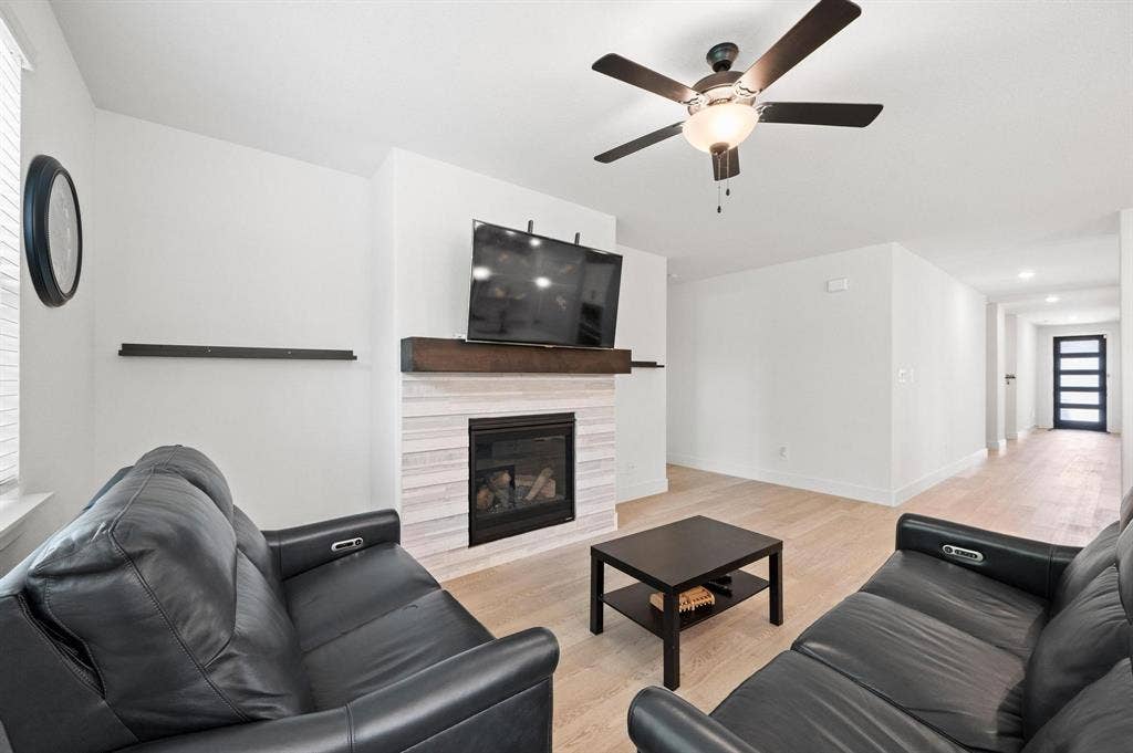 Living area featuring a modern fireplace with a wood-finish mantel, light wood-finish flooring, and a ceiling fan with integrated lighting