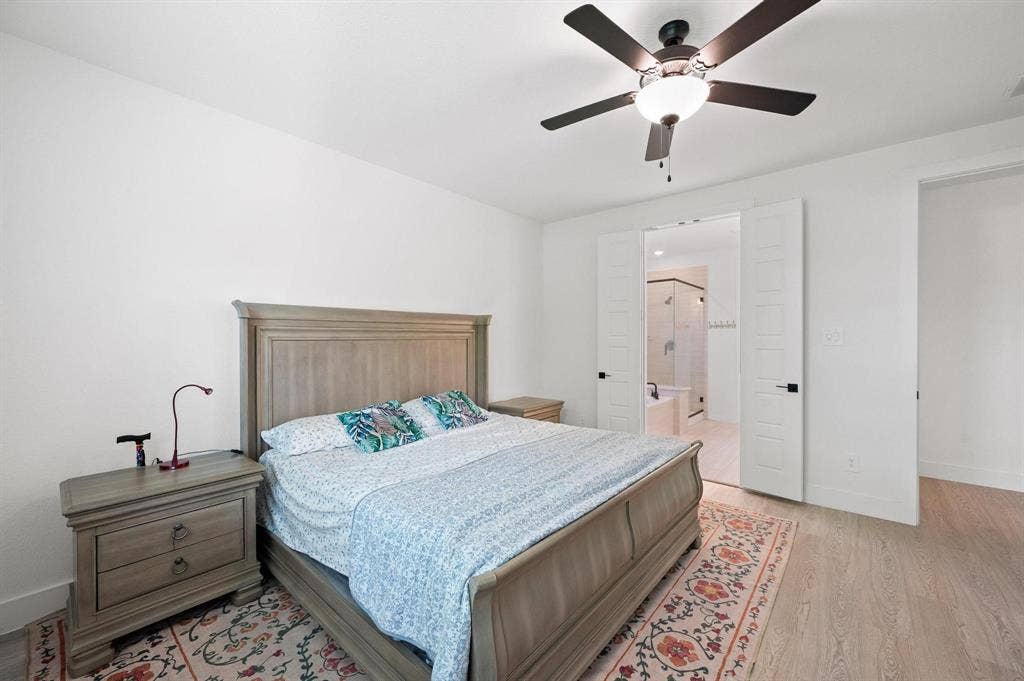Light wood-finish flooring, ceiling fan with integrated lighting, white walls, and double pocket doors leading to an adjacent bathroom