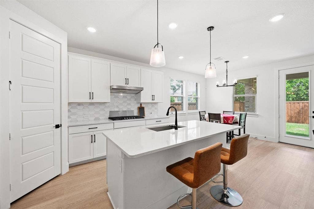 Modern kitchen featuring white cabinetry, a white countertop island, stainless steel range hood, light wood-finish flooring, and a glass-paneled back door