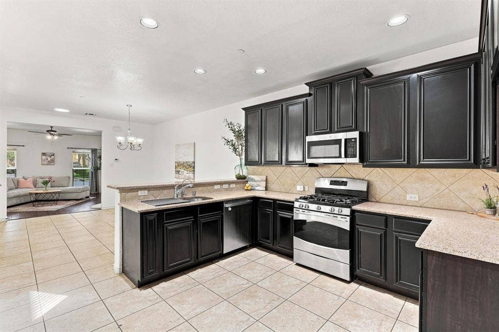 5605 Cojimar Drive, McKinney, TX 75070 Kitchen featuring dark wood cabinetry, light speckled countertops, stainless steel appliances, and a tiled backsplash