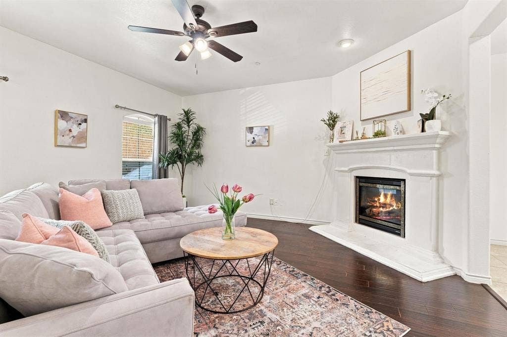 5605 Cojimar Drive, McKinney, TX 75070 Living area featuring dark wood-finish flooring, a white mantel fireplace with a hearth, and a ceiling fan with integrated lighting