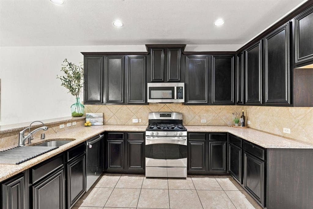 5605 Cojimar Drive, McKinney, TX 75070 Kitchen featuring dark wood cabinetry, light speckled countertops, a tile backsplash, stainless steel appliances, and tile flooring