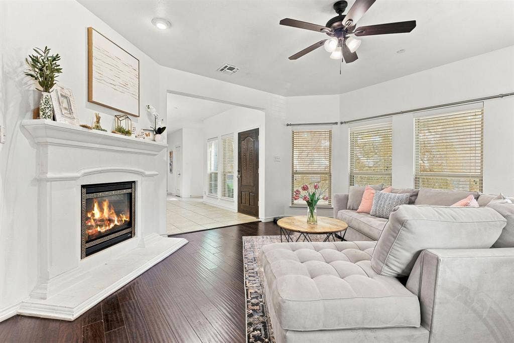5605 Cojimar Drive, McKinney, TX 75070 Hardwood flooring, recessed lighting, ceiling fan, white mantel fireplace, and multiple windows with blinds