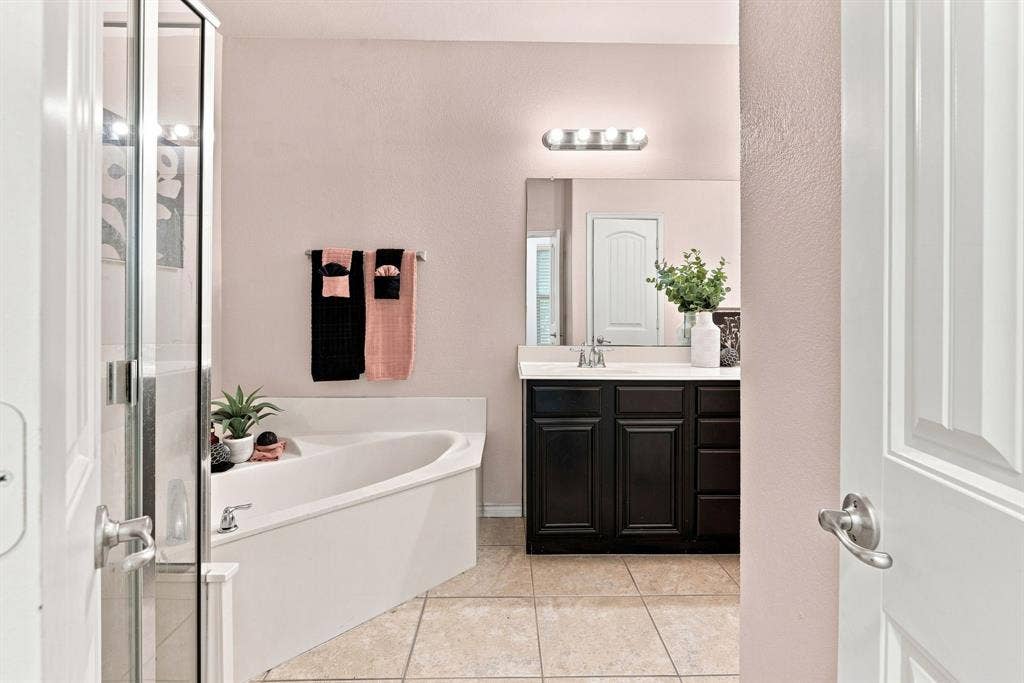5605 Cojimar Drive, McKinney, TX 75070 Built-in corner tub, glass-enclosed shower, single vanity with dark wood cabinetry, integrated sink, and large wall-mounted mirror