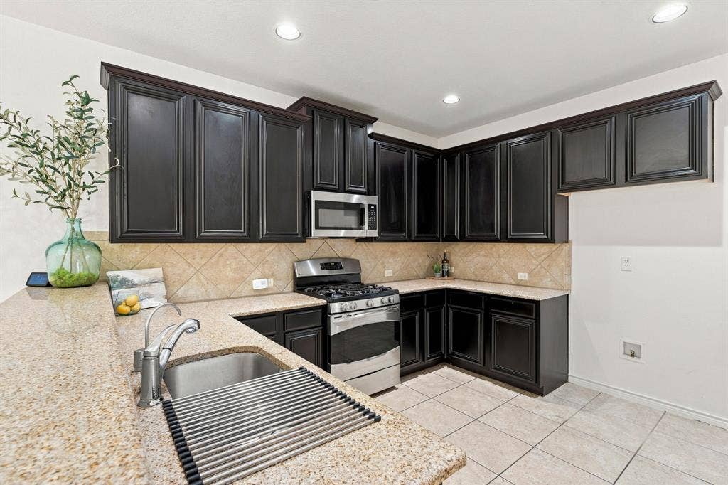 5605 Cojimar Drive, McKinney, TX 75070 Kitchen featuring dark wood cabinetry, light-toned countertops, stainless steel appliances, a tile backsplash, and recessed lighting